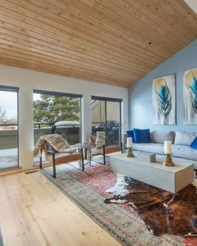Modern living room with wood ceiling, fireplace, wall-mounted TV, and mountain views through large windows