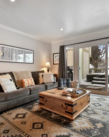 Open-plan loft with gray sofa, leather chair, wooden coffee table, and mezzanine level with black metal railings above kitchen area.