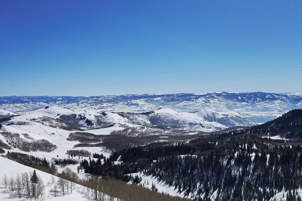 Panoramic view from Park City ski resort looking out over snow-covered valley and mountain ridgelines under a deep blue sky