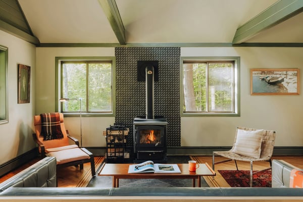 Clean mountain cabin living room with wood stove, vaulted ceiling with exposed beams, and warm natural light