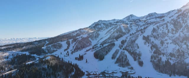 Aerial view of a Utah ski resort on a clear winter day, ski runs cutting through pine forest down a sunlit mountain face